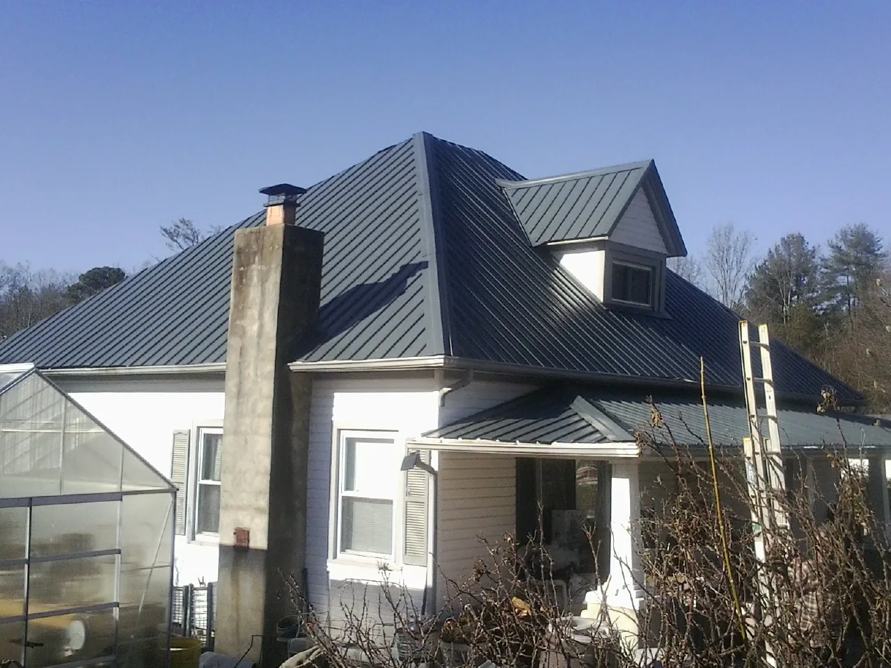 Dark blue standing seam metal roof on a white farmhouse with dormer — Slate & Tile Roof Repair by Roofing Brothers in Lawton