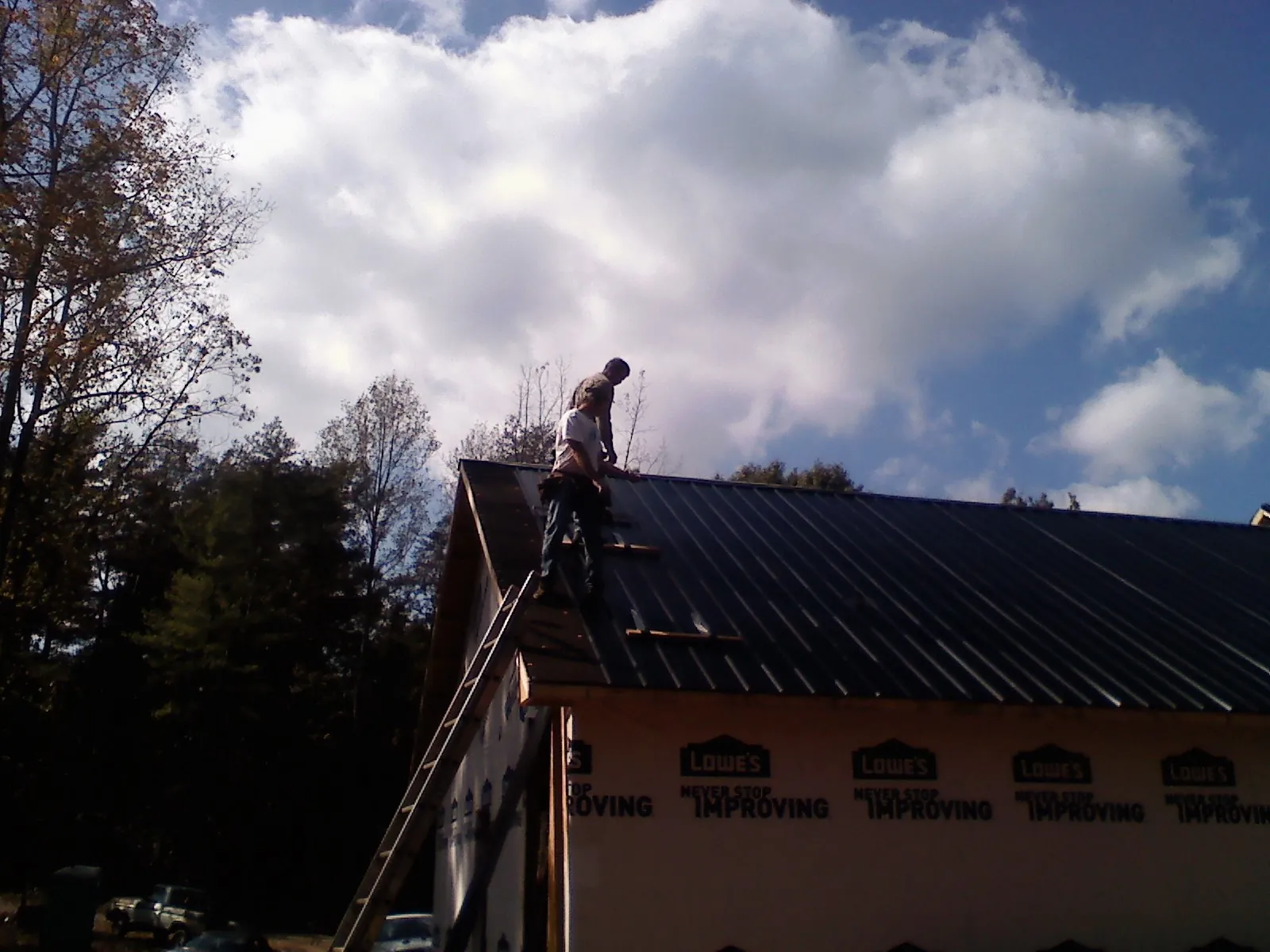 Roofer fastening dark metal panels high against a cloudy sky in Lawton